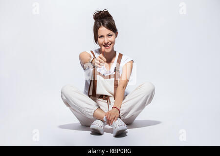 Bella giovane donna seduta sul pavimento, sorridente positivo, facendo segno OK con la mano e le dita. Espressione di successo Foto Stock