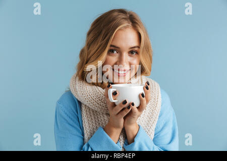 Immagine di carino donna 20s avvolto in una sciarpa sorridente e bicchiere di contenimento con tè o caffè isolate su sfondo blu Foto Stock