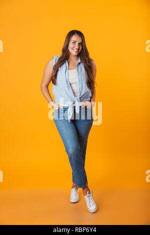 A piena lunghezza Ritratto di una giovane sorridente sovrappeso woman standing isolate su sfondo giallo Foto Stock