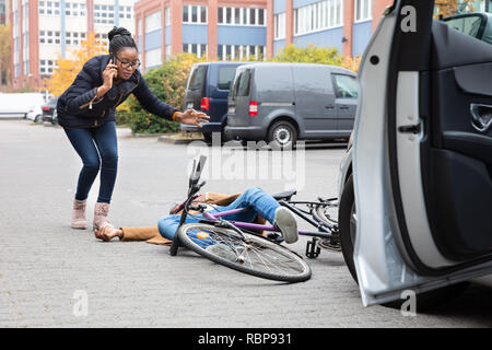 Giovane donna chiamando ambulanza dopo colpire ciclista maschio accidentalmente con la sua automobile Foto Stock