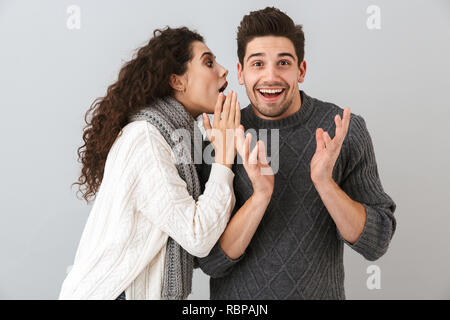 Ritratto di donna eccitato a parlare con il suo ragazzo nel suo orecchio isolate su uno sfondo grigio Foto Stock