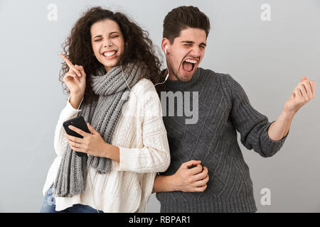 Ritratto di giovane giocoso l uomo e la donna l'ascolto di musica con cuffie e dancing isolate su uno sfondo grigio Foto Stock