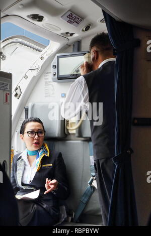 Uno del Kazakistan airlines equipaggio si prepara per il volo con porta principale ancora aperta, due assistenti di volo la preparazione di bloccare l'aereo porta l uomo parlando telefono. Foto Stock