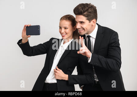 Ritratto di un felice giovane azienda giovane che indossa abiti prendendo un selfie isolate su uno sfondo grigio Foto Stock