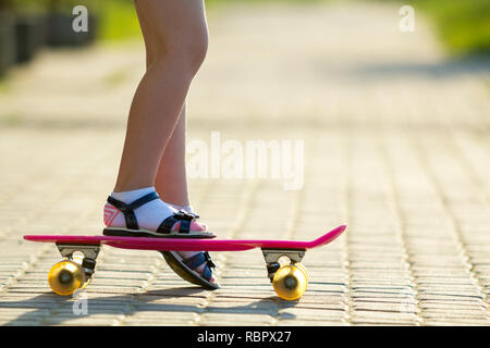 Bambino gambe slim in calze bianche e sandali nero sulla plastica rosa su skateboard luminosa estate copia sfocata spazio sullo sfondo della pavimentazione. All'aperto ac Foto Stock