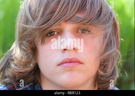 Un close up ritratto di un ragazzo youg con capelli lunghi guardando la fotocamera. Foto Stock