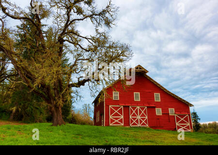 Un vecchio granaio rosso si siede su una collina di un rifugio della fauna selvatica nelle zone rurali Oregon sotto la mattina presto il cielo nuvoloso. Foto Stock