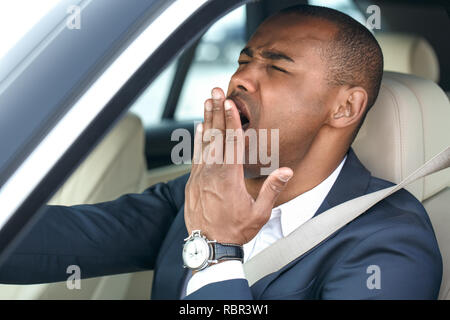 Giovane imprenditore mulatto guidatore seduto all'interno della guida auto sbadigli che copre la bocca con la mano stanco vista nella finestra aperta di close-up Foto Stock