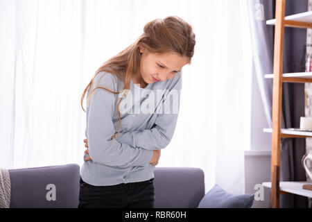 Ragazza in piedi nella parte anteriore del divano avente mal di stomaco Foto Stock