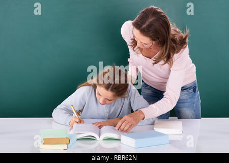 Insegnante femminile aiutando il suo studente facendo il lavoro in classe in aula Foto Stock