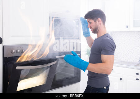 Paura giovane uomo Guardando il fuoco che esce dal forno in cucina Foto Stock