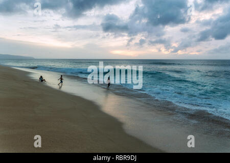 Le persone che giocano sulla spiaggia con grandi onde sulla North Shore di Oahu, Hawaii Foto Stock