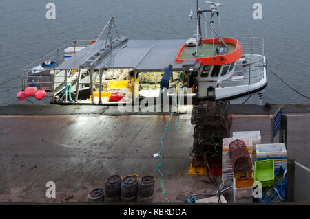 Il caricamento di una barca da pesca con pentole di granchio al tramonto a Wells quay sulla Costa North Norfolk Foto Stock