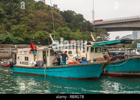 Hong Kong, Cina - 12 Maggio 2010: primo piano della piccola pesca in barca in porto. Altre navi ormeggiate intorno a. Due uomini la preparazione della nave. La vegetazione verde Foto Stock