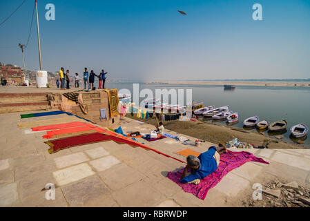 La vita lungo il Gange a Varanasi: uomo giace su un foglio in wintery sunshine mentre i ragazzi volare Kites in una distanza. Varanasi, India Foto Stock