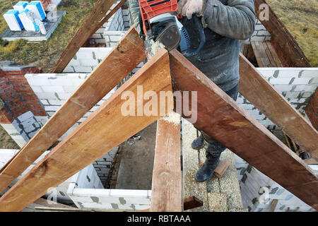 Lavoratori tagliare le travi a vista sul tetto della casa di sega a nastro Foto Stock