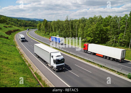 I carrelli che viaggiano su un asfalto autostrada tra foreste. Delle montagne boscose in background. Vista da sopra. Soleggiata giornata estiva. Foto Stock