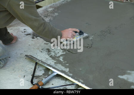 Workman smussa un rivestimento skim di cemento su una vecchia scalinata. Foto Stock