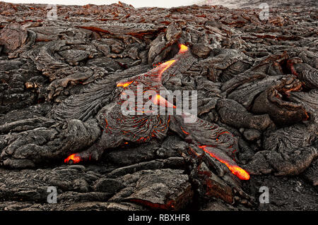 Un flusso di lava emerge da una colonna di terra e scorre in un nero paesaggio vulcanico, nel cielo mostra la prima luce del giorno - Ubicazione: Hawaii, Big Island, Foto Stock