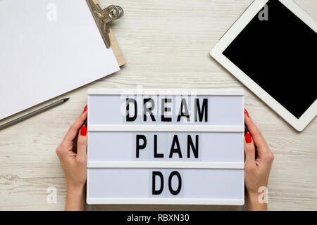 Mani femminili tenere lightbox con il testo 'Dream plan do', appunti, matita e compressa bianca su una superficie di legno, vista dall'alto. Area di lavoro. Da sopra la piana Foto Stock