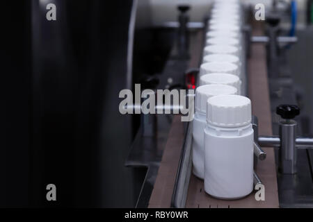 Bottiglia di plastica bianca sulla linea di produzione del nastro alla macchina di riempimento in fabbrica medica. Il fuoco selettivo. Foto Stock