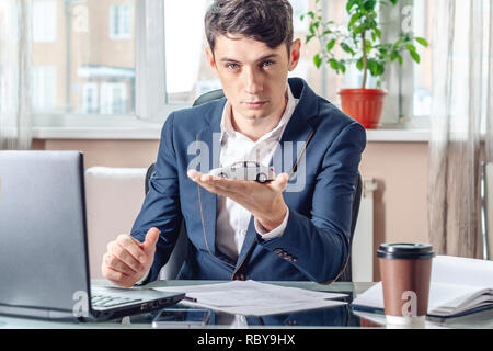 L'uomo agente che tiene un auto giocattolo in ufficio. Il concetto di acquistare vendita e noleggio di trasporto Foto Stock