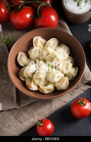 Canederli di carne servita con pomodori e panna acida sulla pietra nera sullo sfondo Foto Stock