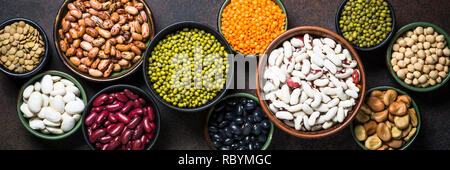 Legumi, lenticchie, chikpea e fagioli assortimento in differenti ciotole sul tavolo di pietra. Lunga formato banner. Foto Stock