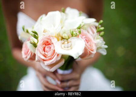 Bouquet nozze nelle mani di un irriconoscibile sposa. Su un bouquet di un paio di oro gli anelli di nozze. Close-up foto. Foto Stock