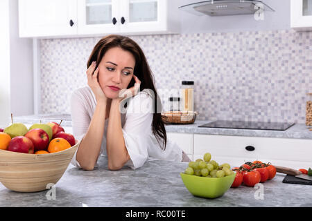 Frutta fresca di fronte sconvolto giovane donna appoggiata sul banco di cucina Foto Stock