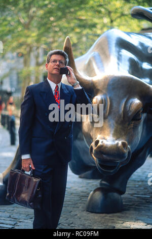 Anni Novanta imprenditore è sul suo telefono cellulare di fronte la carica bull statua, il Quartiere Finanziario di New York City, Stati Uniti d'America Foto Stock