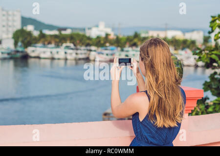 Bellissima giovane donna allegra prendendo un selfie contro lo sfondo del mare e barche vietnamita. Foto Stock