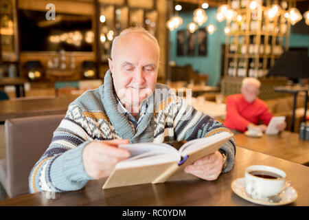 Curioso paffuto uomo la lettura di libri interessanti in cafe Foto Stock