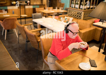Senior positivo uomo che ascolta la musica nelle cuffie Foto Stock