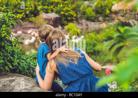 Madre e figlio stanno guardando il gregge di uccelli, di fenicotteri rosa su un laghetto. Foto Stock