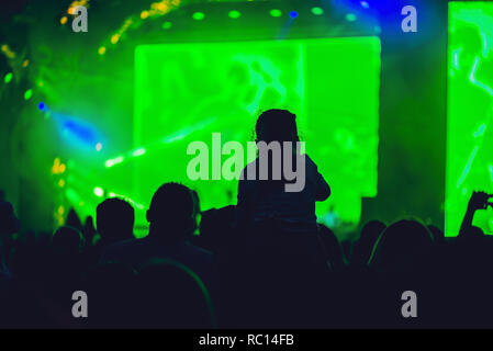 Silhouette di una grande folla al concerto contro una luminosa fase. Tempo di notte concerto rock con persone aventi fun il sollevamento in alto le mani in aria e rasserenanti i musicisti Foto Stock