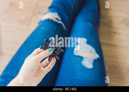 Ragazza adolescente in holey jeans tiene in mano e gioca con un dispositivo a rotazione vorticosa Foto Stock