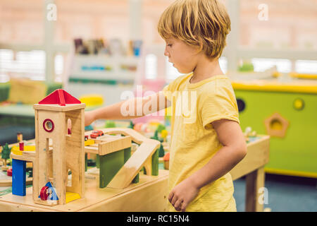 I bambini giocano con il giocattolo di legno, costruire ferrovia giocattolo a casa o asilo nido. Il Toddler boy gioca con gru, treno e auto. Giocattoli educativi per la scuola materna e asilo bambino. Mobili imbottiti, sedia in borsa Foto Stock