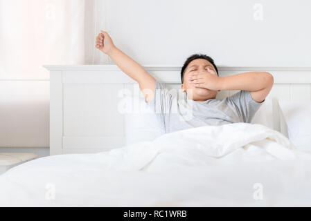 Obesi fat boy wake up sbadigliare e tratto su letto di mattina. concetto pigro Foto Stock