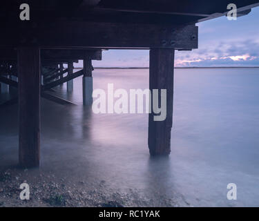 Una lunga esposizione al di sotto di un vecchio ponte di legno, ad alta marea in un freddo inverno mattina. Foto Stock