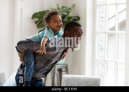 Felice papà africano dà poco figlio piggyback ride a casa Foto Stock