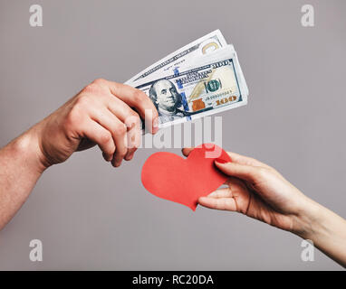 Un maschio di mano che tiene un pacco di denaro per cercare di acquistare un cuore rosso dalla mano femminile - Acquisto di concetto di amore Foto Stock