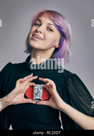 Un rotolo di dollari con il cuore fatto di due mani womans. amore concetto di denaro Foto Stock