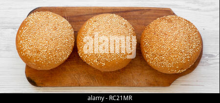 Hamburger freschi panini con semi di sesamo sulla tavola di legno bianco su una superficie di legno, vista aerea. Fast food. Foto Stock