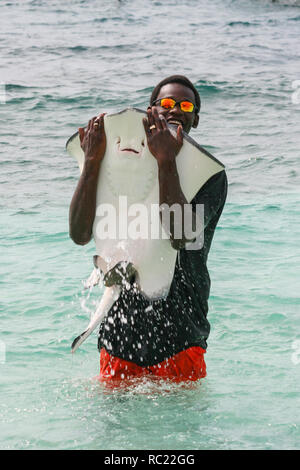 Nassau / Bahamas - Aprile 3.2007: Ritratto di un uomo nero in piedi nel colore turchese acqua holding big stingray pesce sopra l'acqua. Foto Stock