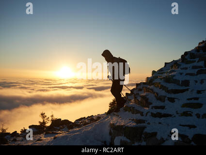 Scalatore turistica con zaino escursionismo sul Monte roccioso ripido pendio coperto con la prima neve sulla copia di sfondo spazio di foggy valley riempito di bianco Foto Stock