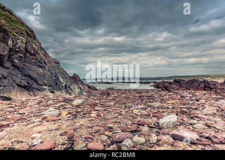 Uno splendido scenario di drammatiche Pembrokeshire litorale,South Wales,Uk.formazioni rocciose sulla spiaggia esposto durante la bassa marea e moody cielo sopra il mare.Scenic. Foto Stock