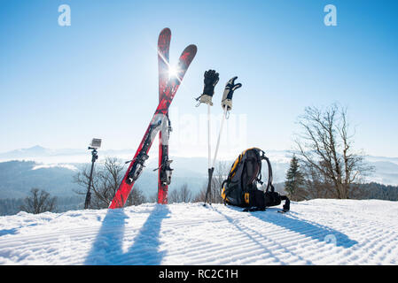 Le attrezzature da sci - sci, zaino, bastoncini, guanti e azione fotocamera su monopiede, sulla parte superiore della pista da sci a ski resort in montagna Foto Stock