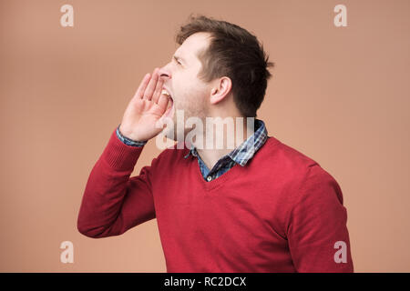 Primo piano vista laterale profilo, ritratto di mad il giovane lavoratore dipendente aziendale con ampia bocca aperta, urlando, isolato su sfondo marrone. Foto Stock