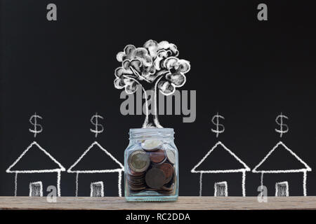 Risparmio di denaro. Gli investimenti di denaro concetti. Home prestito. disegno a mano delle monete di impilamento in un barattolo di vetro e albero in crescita con piccole residenti sulla lavagna. Foto Stock